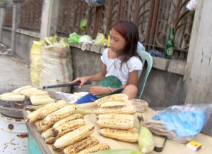 A young girl helps her parents earn a living by selling grilled corn to passersby in Jaro district.