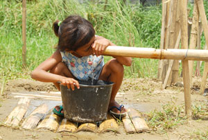 A girl drinks water from an improvised bamboo pipe