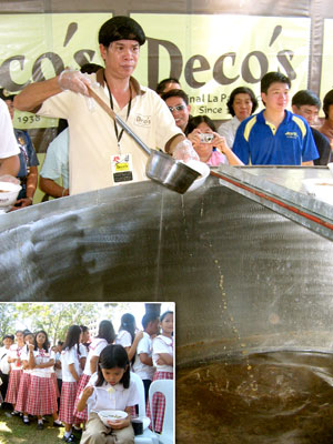 A kitchen crew pours hot soup from a gigantic bowl into a styropore container. 