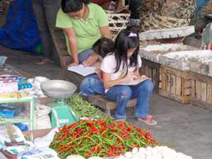 A mother takes time to teach her children to write while tending her merchandise at the Libertad Market in Bacolod City.