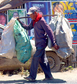 Not minding the weight on his shoulders, this man carries two sacks containing metals and other junk items that he could sell.