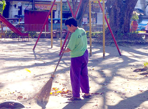 A woman is seen sweeping dried leaves at Plaza Libertad. Trees surrounding the plaza protect her from the afternoon sun.