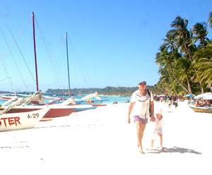 A foreign tourist and his young child walk on the powdery white sand of Boracay island.